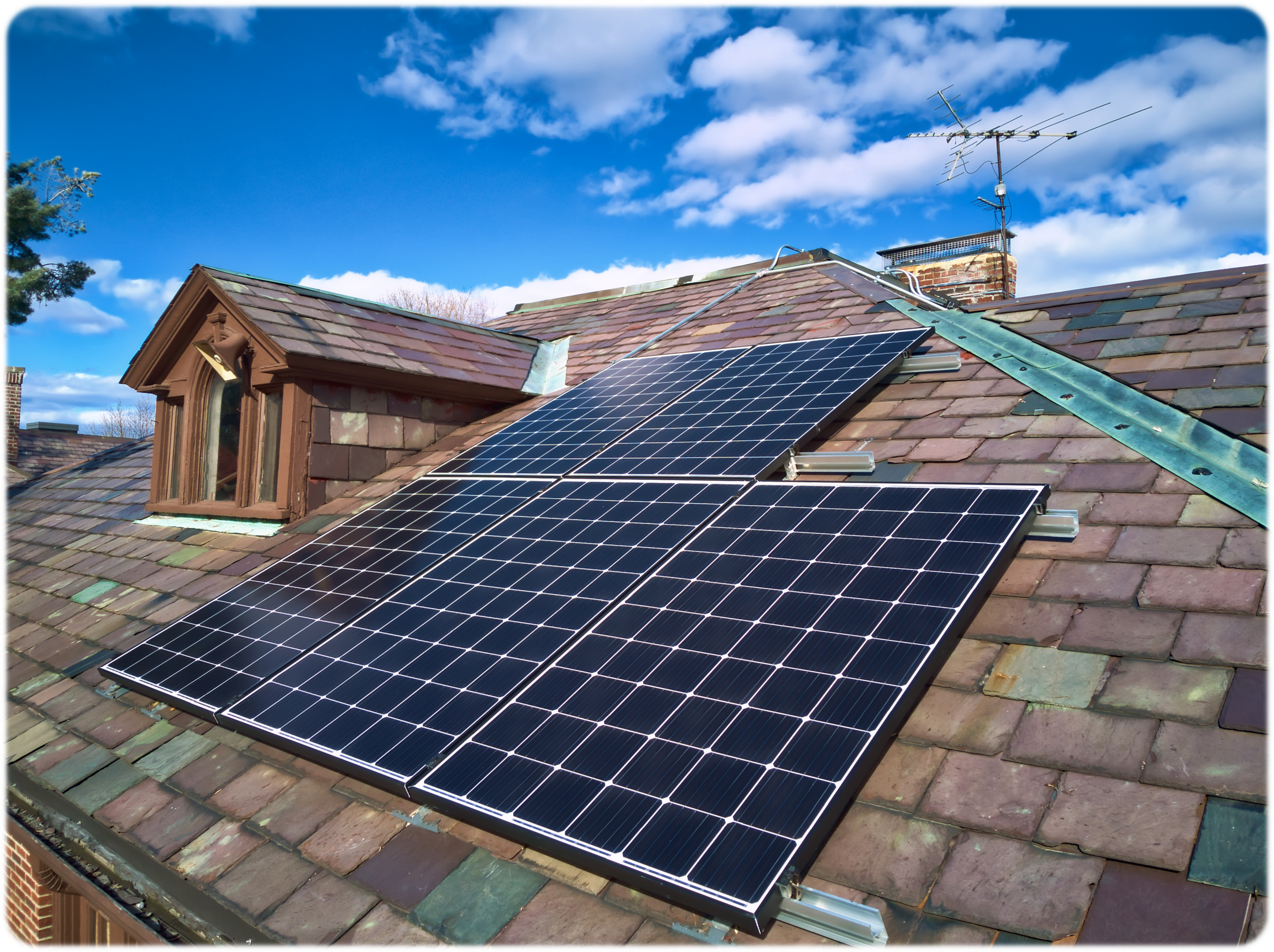 Solar panels mounted on the variegated slate roof of a historic Boston home, with the original slate and Gothic dormer intact