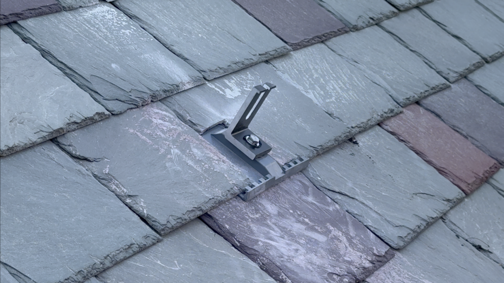Close-up of a SlatePlate mounting bracket installed on a variegated slate roof.